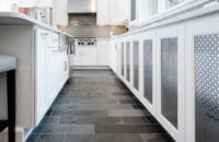 A row of white base cabinets in the kitchen with sleek metal cabinet door inserts.