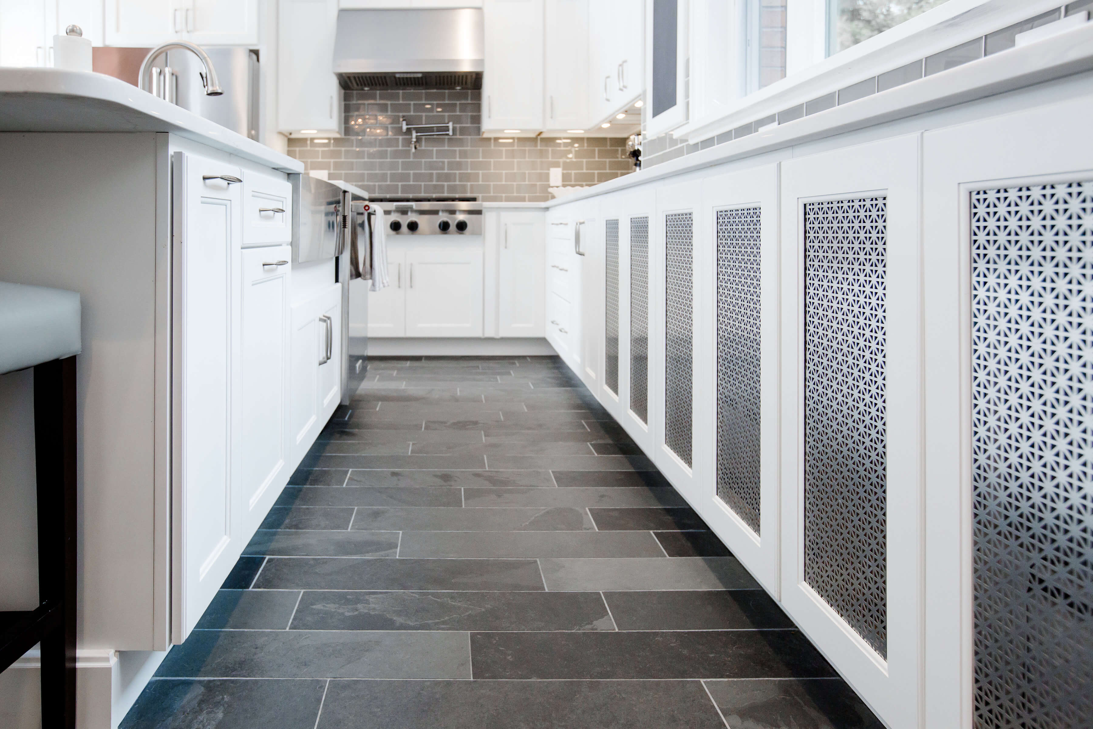 A row of white base cabinets in the kitchen with sleek metal cabinet door inserts.