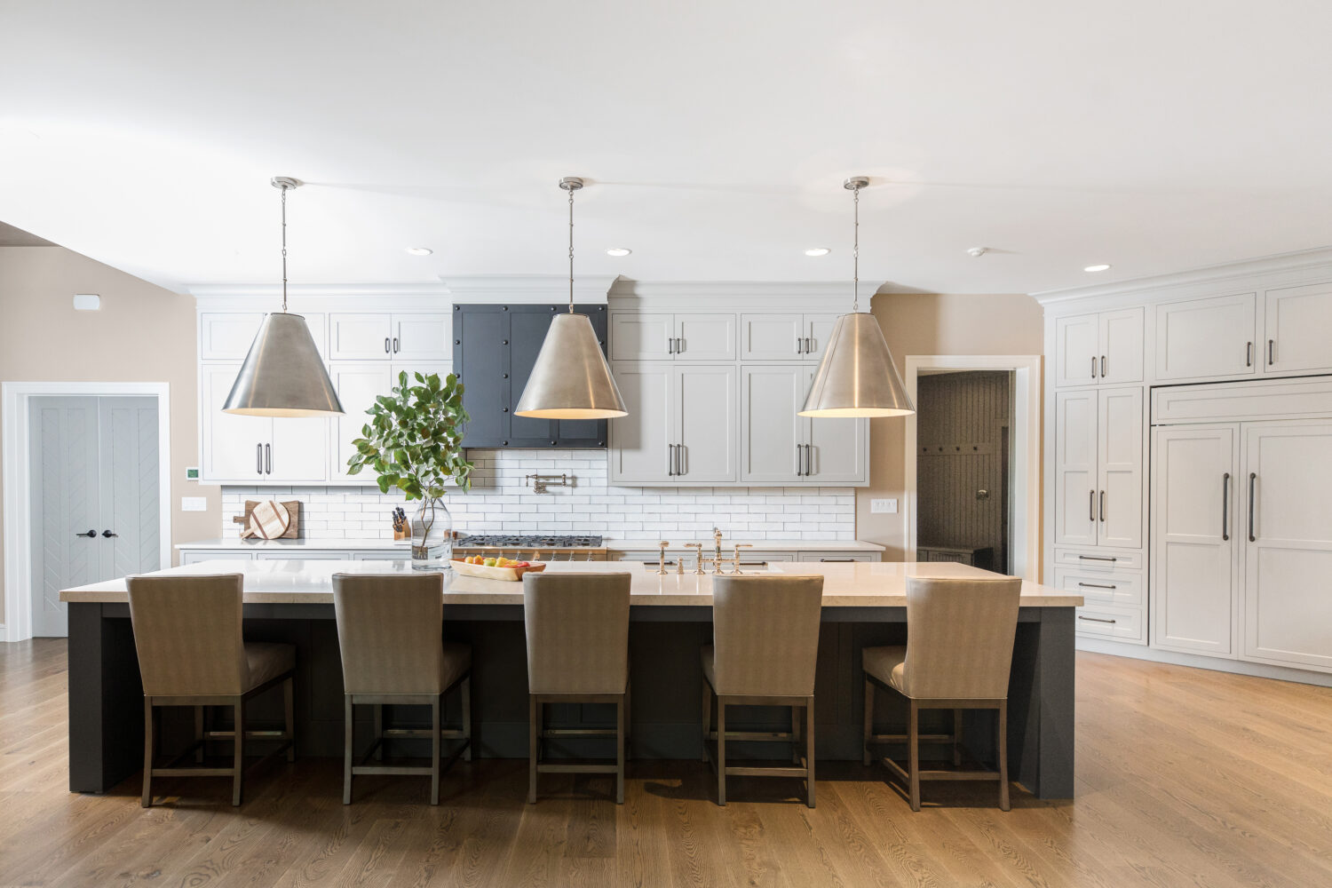 A straight on view of a transitional gray and white kitchen remodel with a long dark gray kitchen island with seating for 5 or 6 surrounded by white painted shaker cabinets.