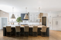 A straight on view of a transitional gray and white kitchen remodel with a long dark gray kitchen island with seating for 5 or 6 surrounded by white painted shaker cabinets.