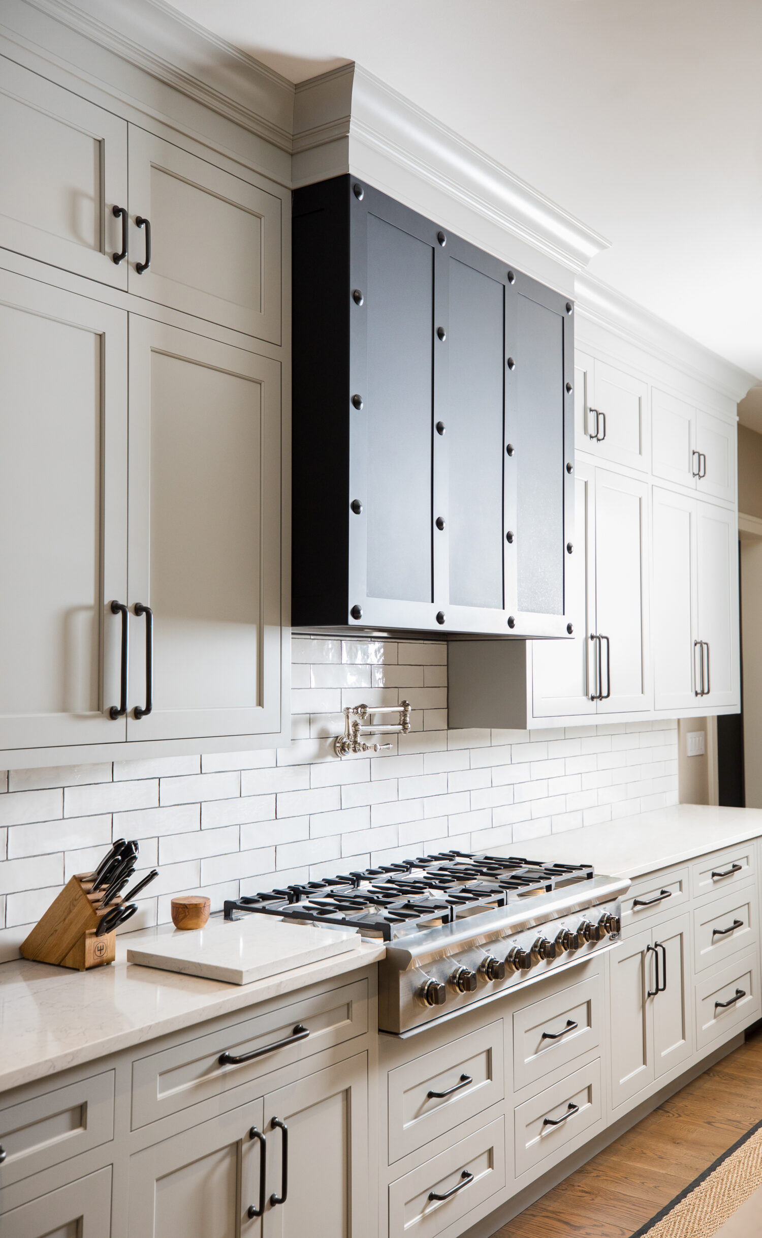 A remodeled kitchen with white shaker cabinet doors, white subway tiles and a dramatic, dark metal range hood.