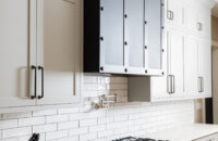 A remodeled kitchen with white shaker cabinet doors, white subway tiles and a dramatic, dark metal range hood.