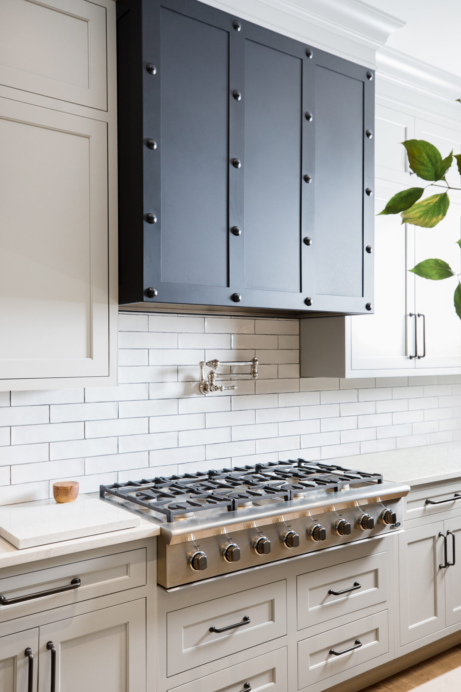 A remodeled kitchen with white shaker cabinet doors, white subway tiles and a dramatic, dark metal range hood.