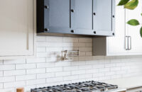 A remodeled kitchen with white shaker cabinet doors, white subway tiles and a dramatic, dark metal range hood.