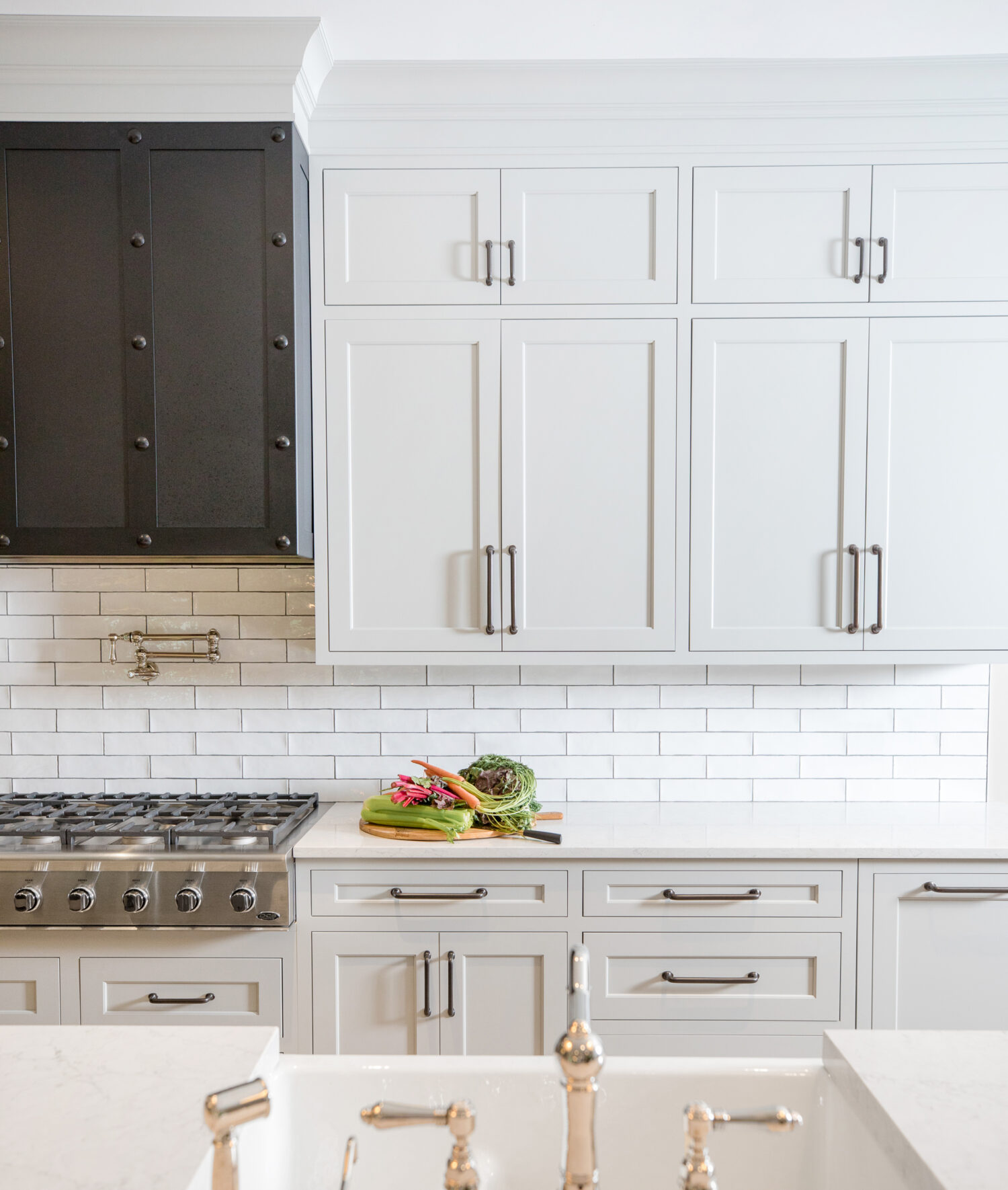 A stunning all white kitchen design with white painted inset shaker cabinets, long dark nickel hardware pulls, white subway tiles, white quartz countertops and a stunning dark metal hood.