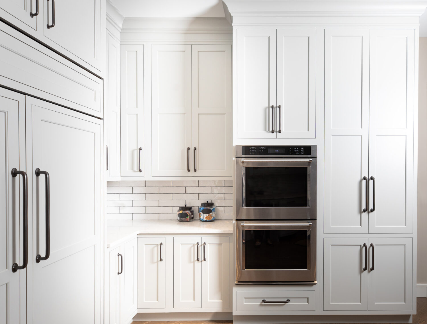 This corner of the kitchen has counter space set into the corner next to a wall of cabinetry that houses the double wall ovens as well ask storage for baking supplies and pantry goods.