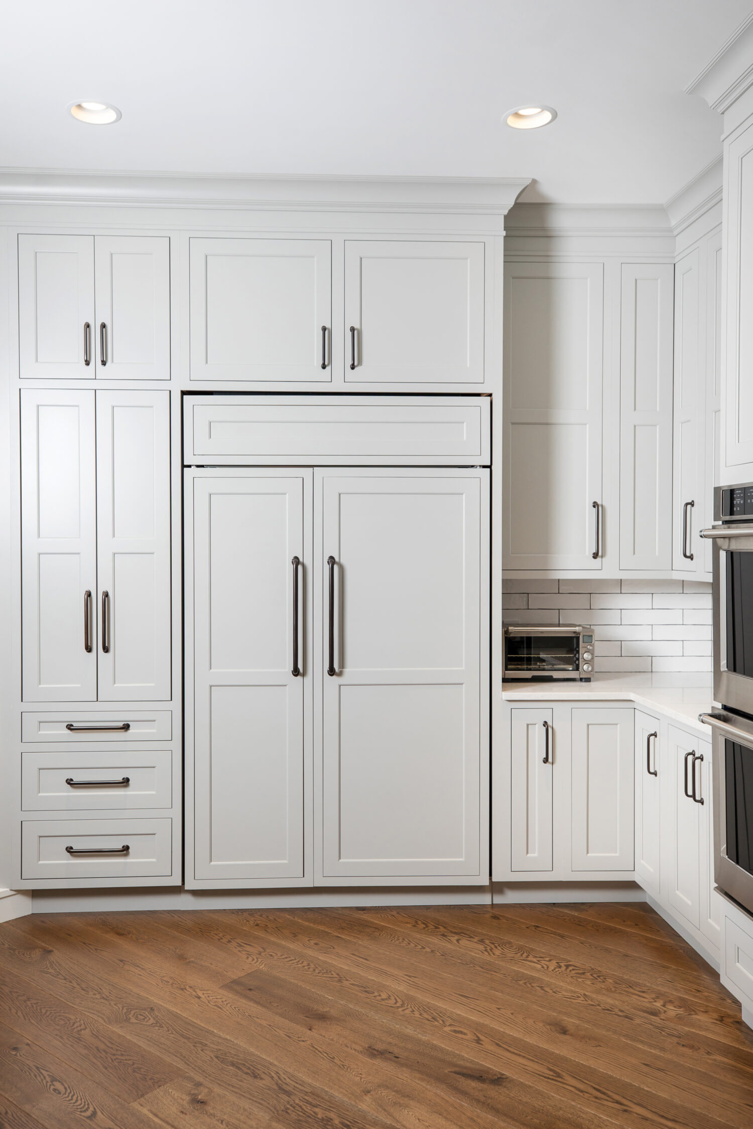 A straight on view of a full wall of cabinets with a concealed paneled refrigerator hidden by cabinet appliance panels from Dura Supreme.