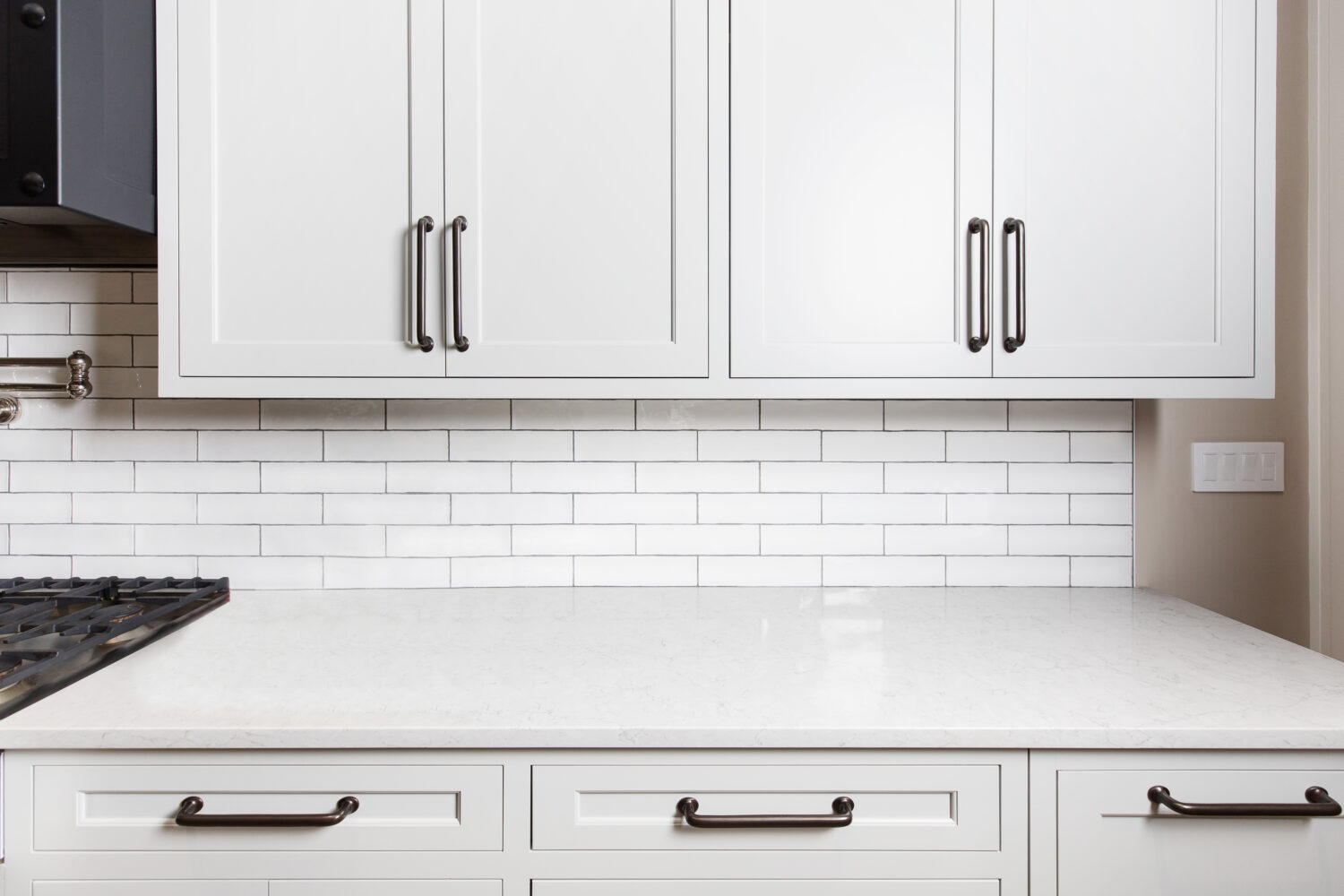A close up view of thin shaker cabinets with a white painted finish, a white quartz countertop, and the simple white subway tile backsplash.