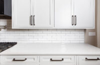 A close up view of thin shaker cabinets with a white painted finish, a white quartz countertop, and the simple white subway tile backsplash.