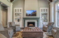 The cabinets flanking the fireplace have a white paint and delicate glass doors. The painted fireplace mantel has a dark green paint color.