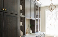 A dark gray stained oak butler's pantry with metal inserts in the doors for a decorative display of the homeowner's serveware collection.