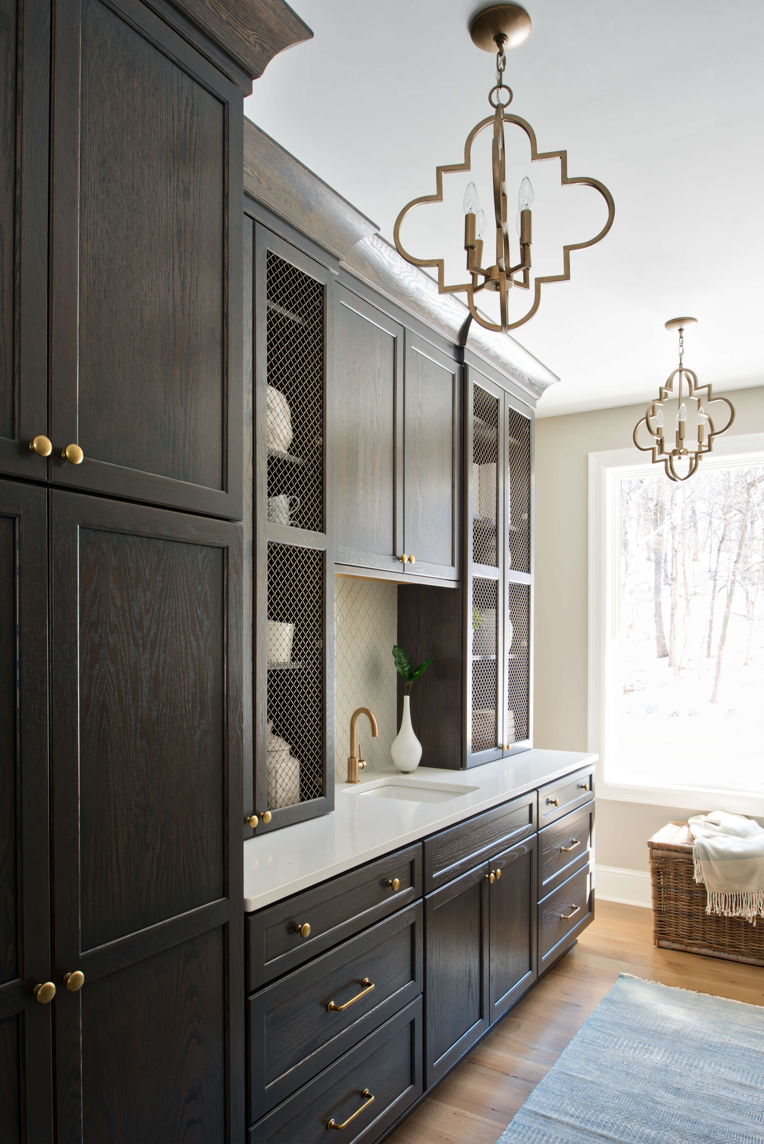 A dark gray stained oak butler's pantry with metal inserts in the doors for a decorative display of the homeowner's serveware collection.