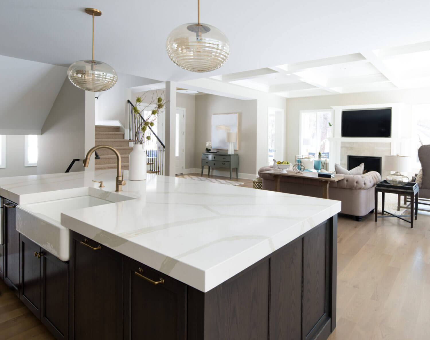 A view over the dark gray stained kitchen island with oak cabinetry into the adjacent living room with a white painted fireplace mantel that coordinated with the White cabinets of the kitchen perimeter.