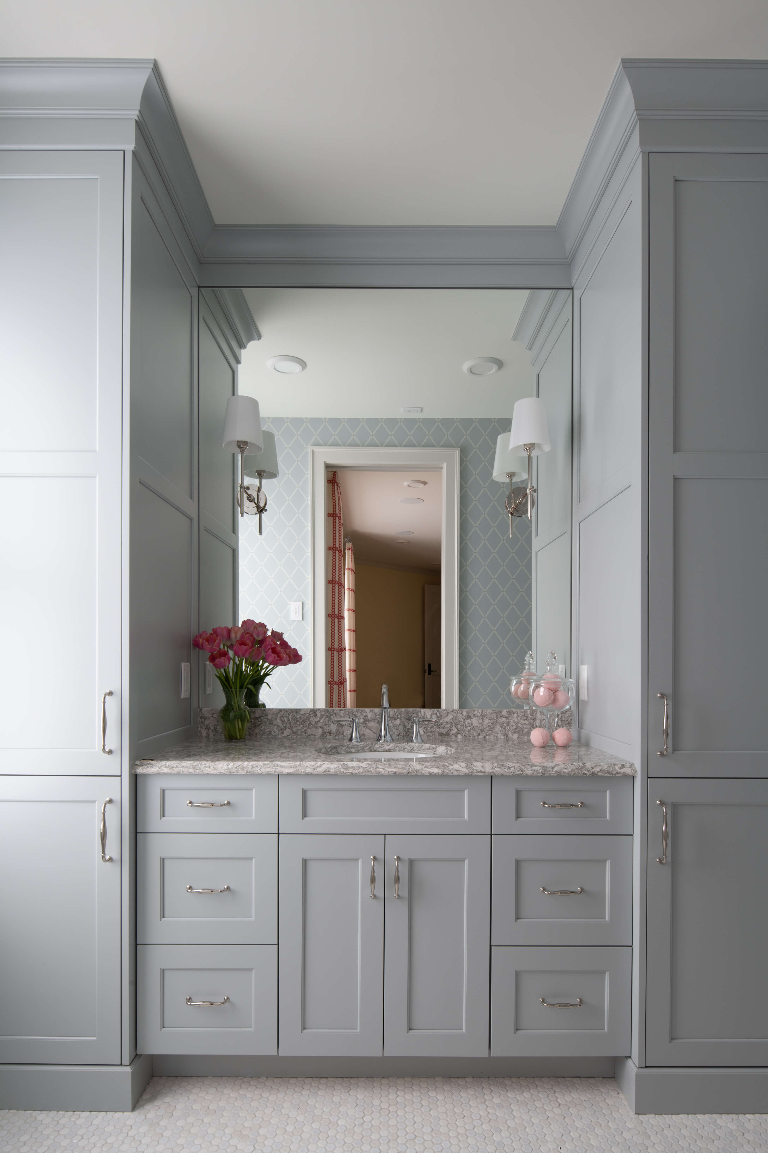 A soft, light gray painted bathroom vanity with two tall linen cabinet towers on both sides of the vanity creating a very symmetrical design.
