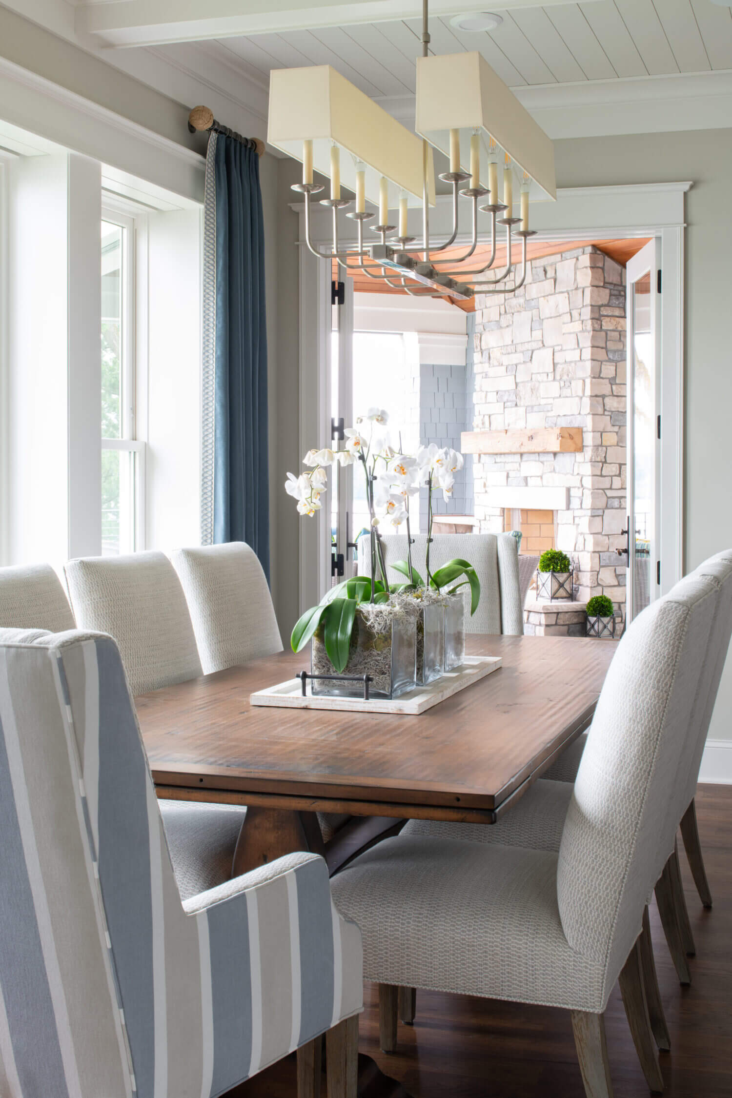 A coastal inspired modern farmhouse dining room with a long chandelier and wood table.