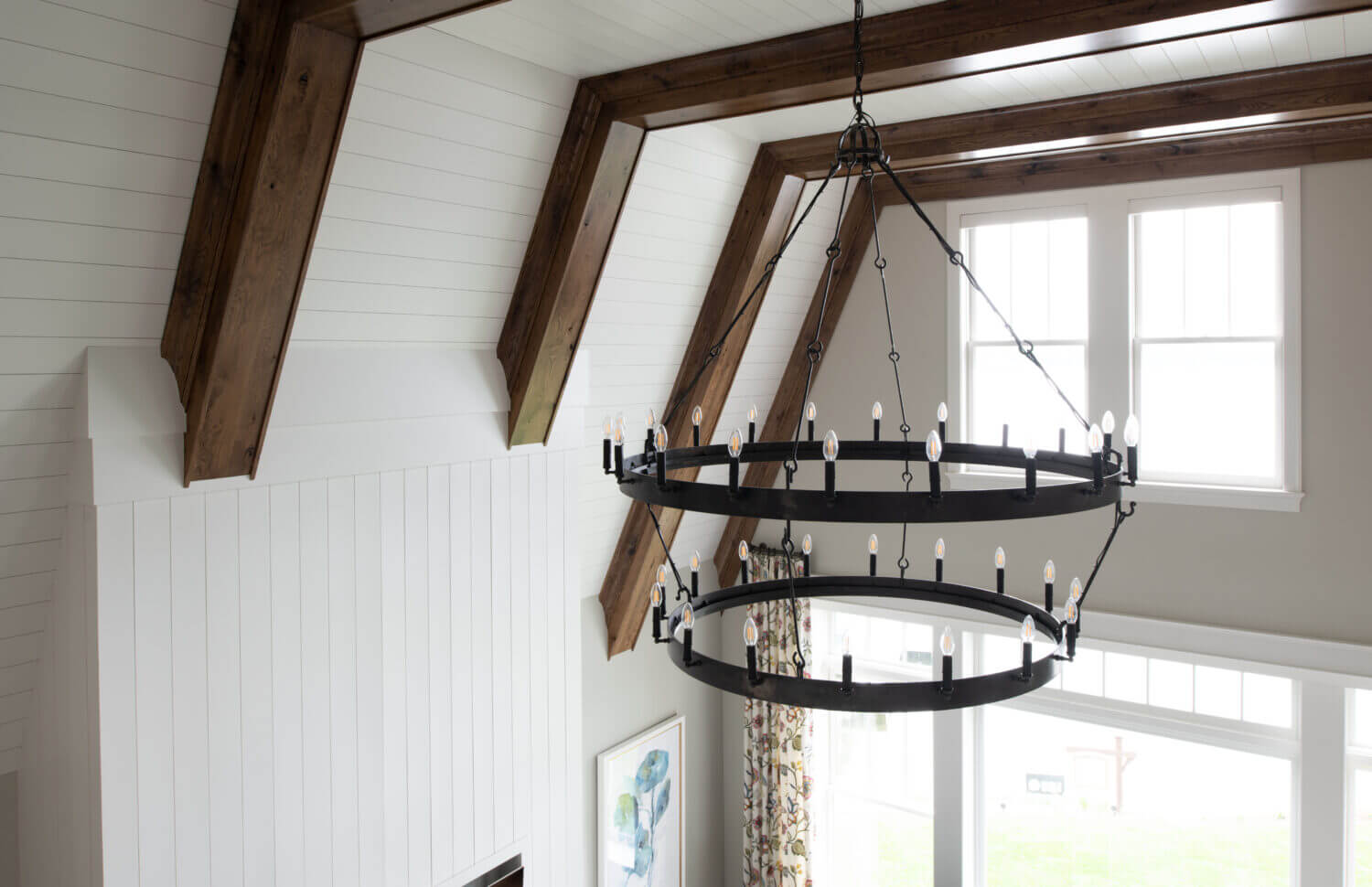 A close up unique vaulted ceilings with large beams and shiplap detail with a large black chandelier light fixture.