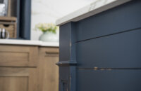 A close up of the kitchen island end cap with shiplap panels and a decorative column with a distressed navy blue painted finish.