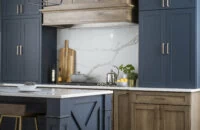 An elegant modern farmhouse remodeled with navy blue and hickory wood cabinets with a hickory wood hood and a kitchen island with an X-shaped end cap and shiplap details.