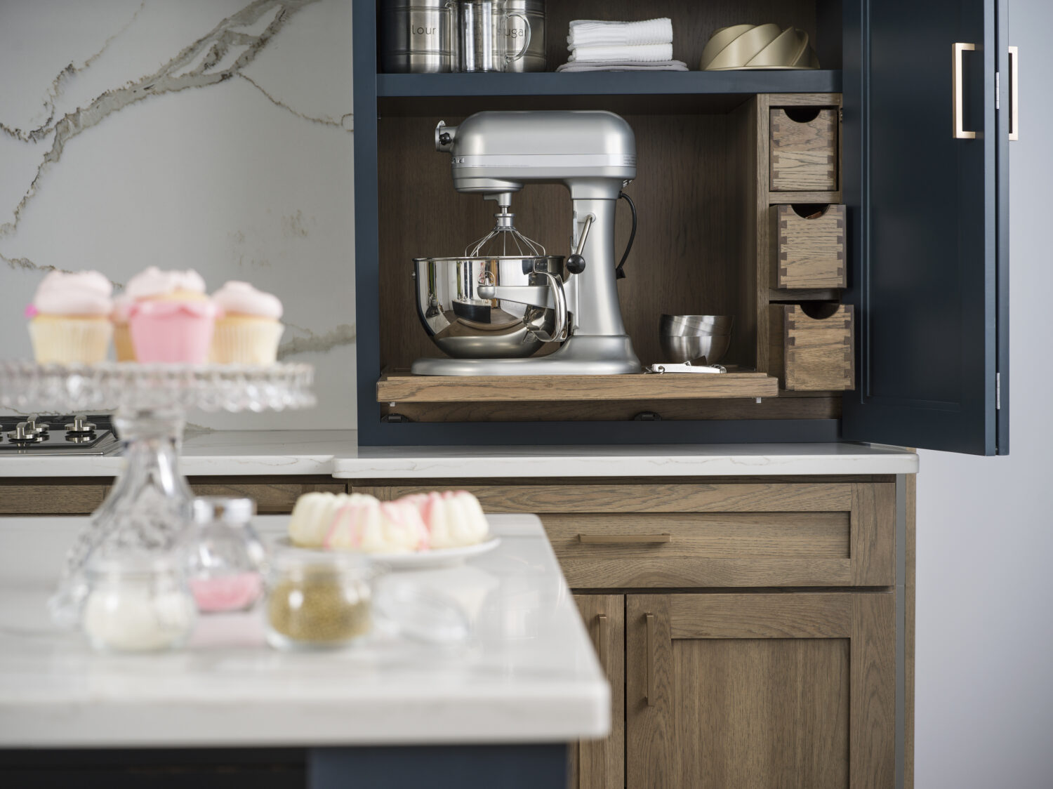 A counter-sitting cabinet opens up to show a larger mixer on a flat roll-out shelf with apothecary storage to the side for misc. storage for baking tools & supplies.