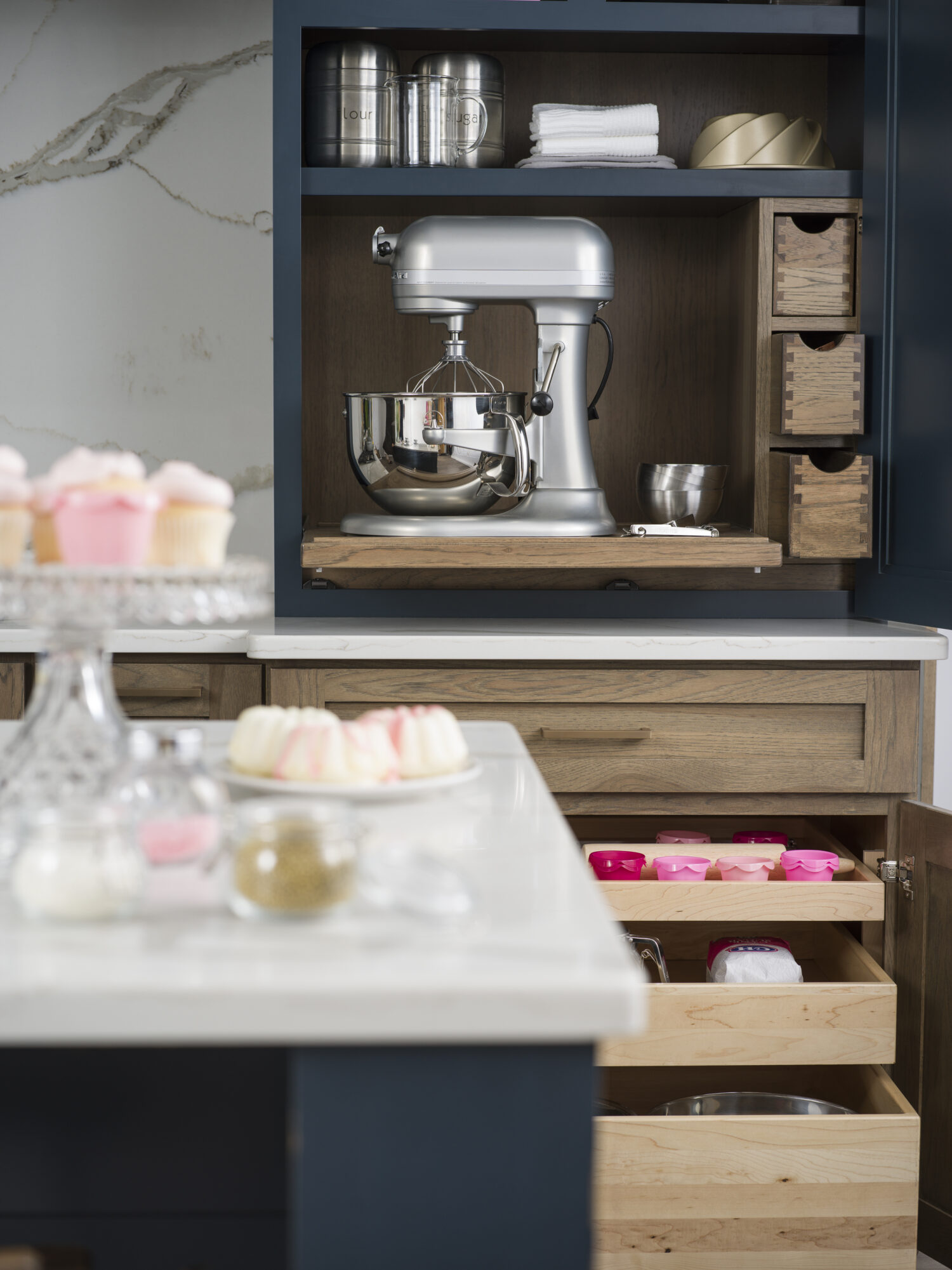 A customized baking station in the kitchen with a large mixer on a flat roll-out shelf and a cabinet below with several roll-out selves in multiple sizes.