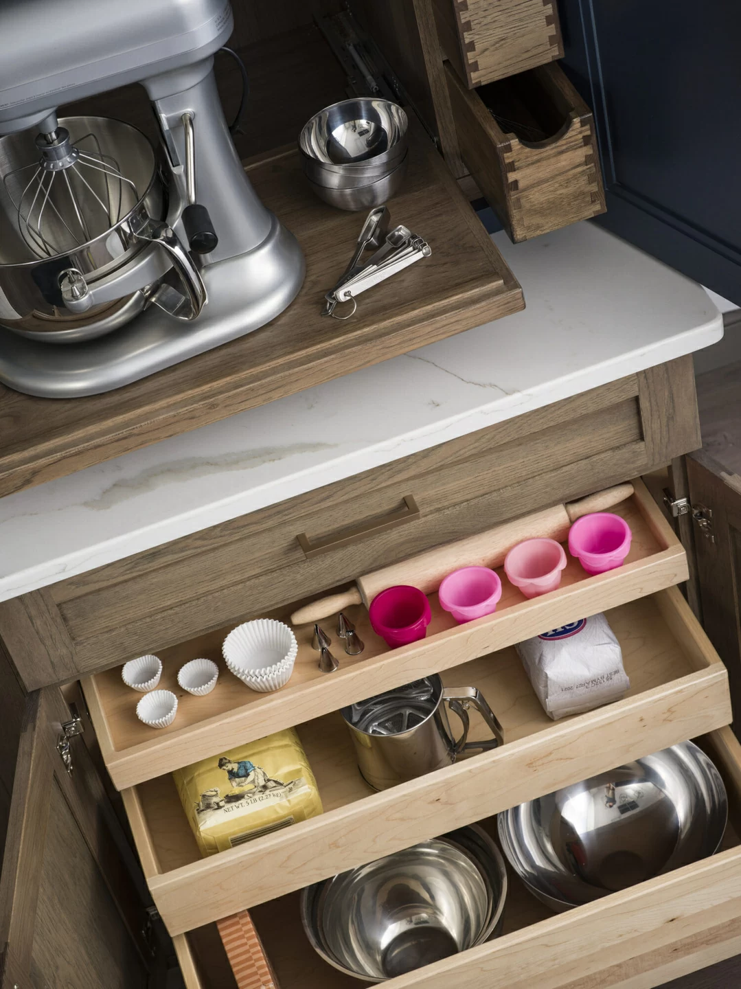 A baking center in the kitchen opens up with several roll-out shelves in multiple sizes for storing baking supplies and a large mixer.