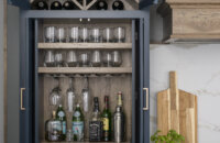 A home bar larder cabinet with a wine glass rack,, appothacary drawers, a roll-out shelf, glassware storage and wine racks above.