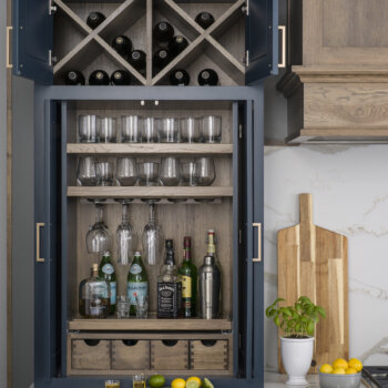 A home bar larder cabinet with a wine glass rack,, appothacary drawers, a roll-out shelf, glassware storage and wine racks above.