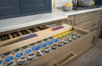 A kitchen drawer opens to show two layers of tiered storage. The top tier has a utensil organizer and storage for tea bags, the bottom is a full drawer K-cup organizer.