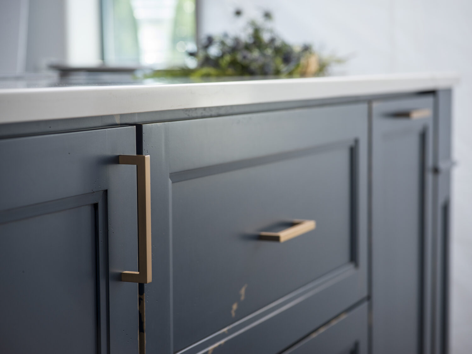 A close up of a distressed painted finish on kitchen cabinets with a dark navy blue color and brass hardware.