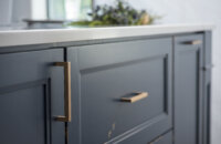 A close up of a distressed painted finish on kitchen cabinets with a dark navy blue color and brass hardware.