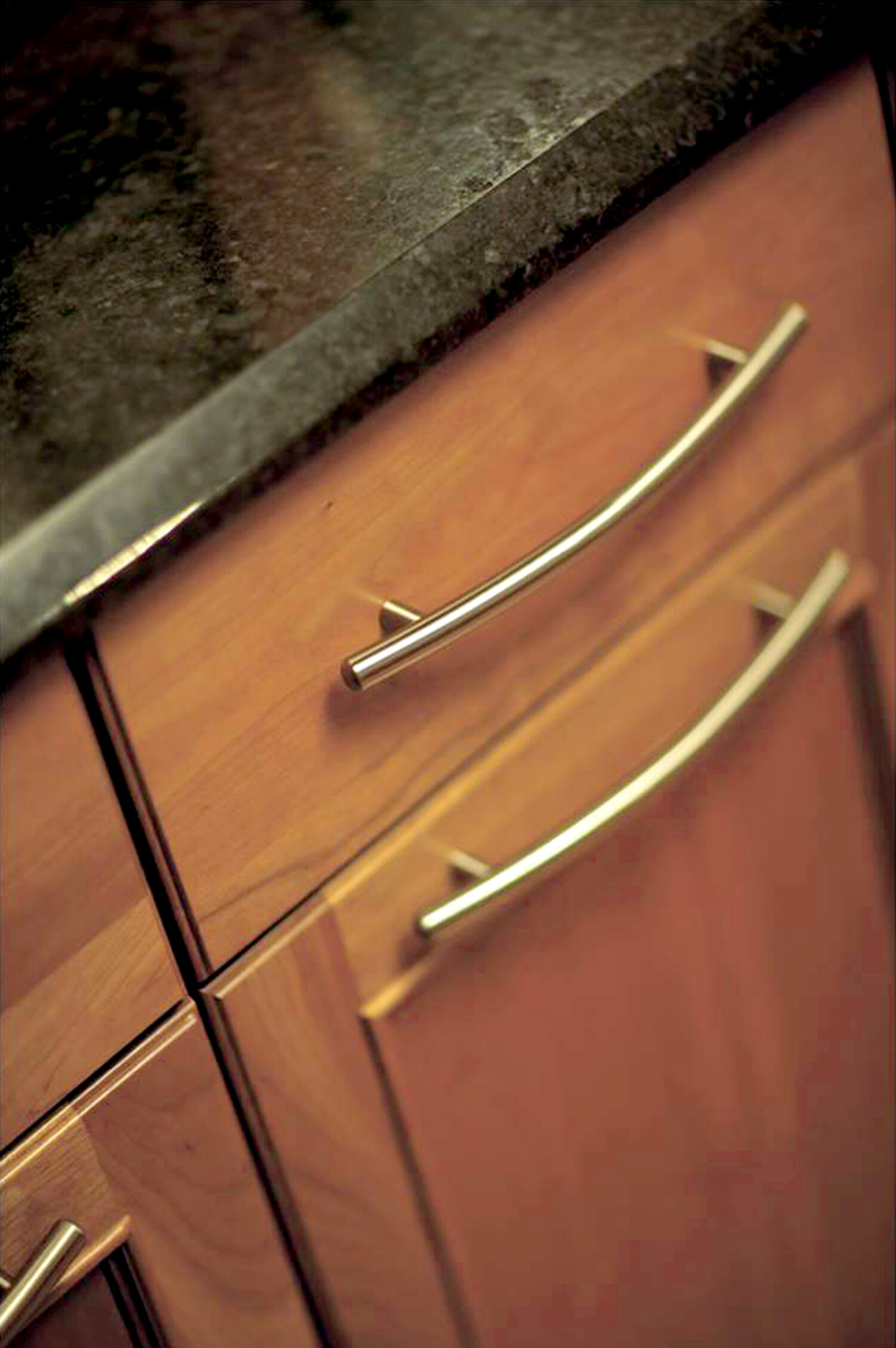A close up to casual style cabinets with a warm stain on cherry wood with a black countertop.