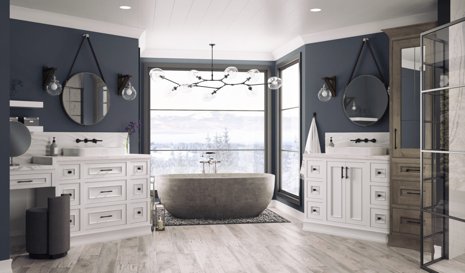 A dream master bathroom with cool navy blue and walls and white painted oak bathroom cabinets and vanities from Dura Supreme. A free standing stone tub sits in front of several large windows with a stunning mountainside view.