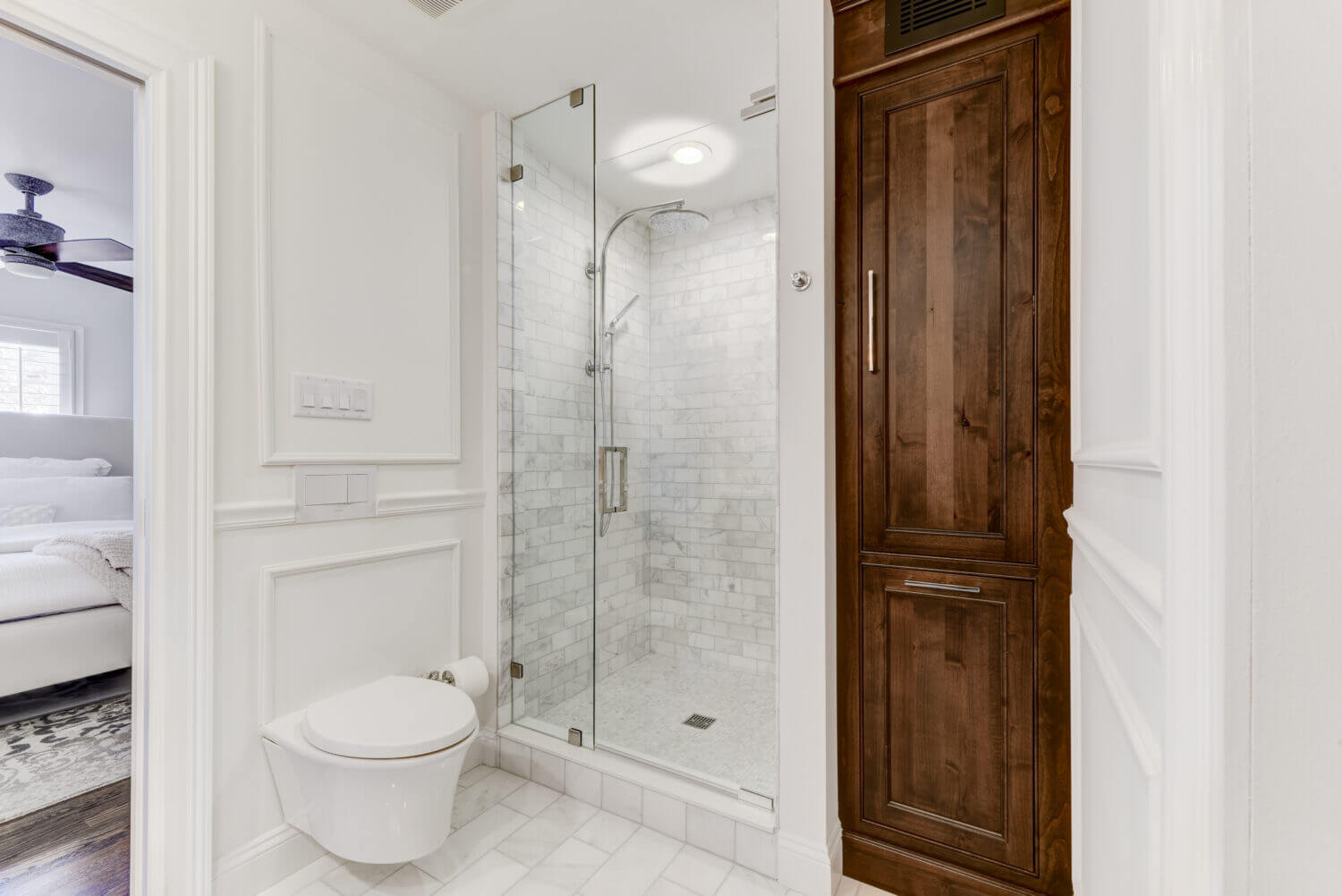 A bright white bathroom with built-in wall inset linen cabinet in a warm stained knotty alder wood. The rustic wood cabinet doors make a beuatiful accent to the all-white color palette.