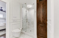 A bright white bathroom with built-in wall inset linen cabinet in a warm stained knotty alder wood. The rustic wood cabinet doors make a beuatiful accent to the all-white color palette.