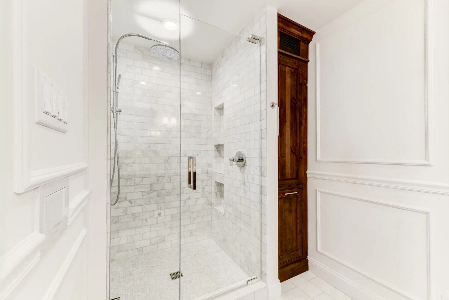 A bright white bathroom with built-in wall inset linen cabinet in a warm stained knotty alder wood. The rustic wood cabinet doors make a beuatiful accent to the all-white color palette.