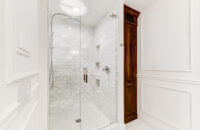 A bright white bathroom with built-in wall inset linen cabinet in a warm stained knotty alder wood. The rustic wood cabinet doors make a beuatiful accent to the all-white color palette.