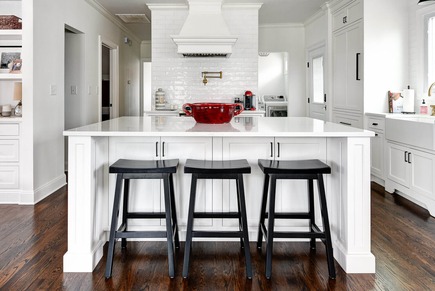 The kitchen island and wood hood create a beautiful center to this kitchen design. The 3 black stools contrast the bright white shaker style cabinets.