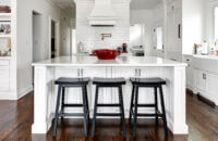 The kitchen island and wood hood create a beautiful center to this kitchen design. The 3 black stools contrast the bright white shaker style cabinets.