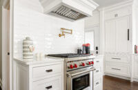 The range an cook top in this remodeled kitchen sits in the center of a the room. The designer highlighted the area with a full wall subway backsplash that surrounds and emphasizes a beautiful white painted wood hood.