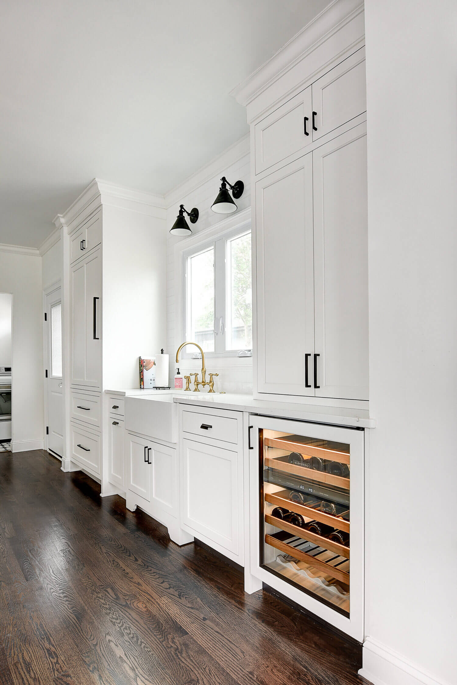 The wall with the sink in this kitchen has a beautiful window view, lots of counter space on both sides of the sink, tons of cabinet storage, and a below counter beverage fridge at the end nearest the dining space.