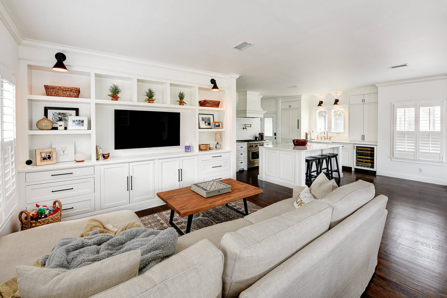 An all white open concept living room and kitchen. The built-in entertainment center matches the bright white shaker kitchen cabinetry.