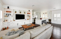 An all white open concept living room and kitchen. The built-in entertainment center matches the bright white shaker kitchen cabinetry.