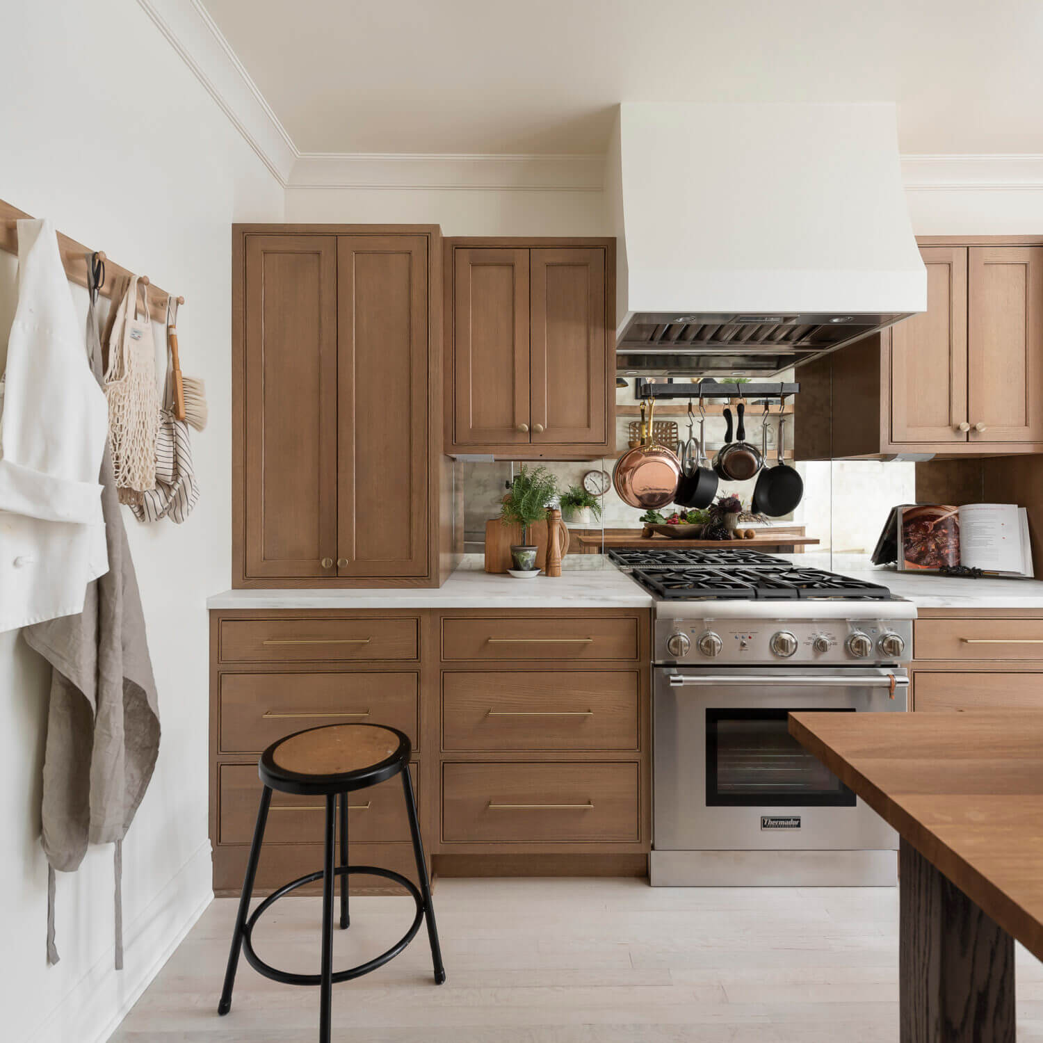 A stunning remodeled kitchen with light stained wood cabinets from Dura Supreme cabinetry. The kitchen also features a bright white modern wood hood and a mirror backsplash.