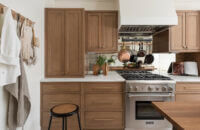 A stunning remodeled kitchen with light stained wood cabinets from Dura Supreme cabinetry. The kitchen also features a bright white modern wood hood and a mirror backsplash.