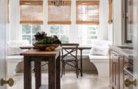 A look from the kitchen, over the small weathered kitchen island table into the dining room space with a bright white built-in breakfast nook with banquette seating.