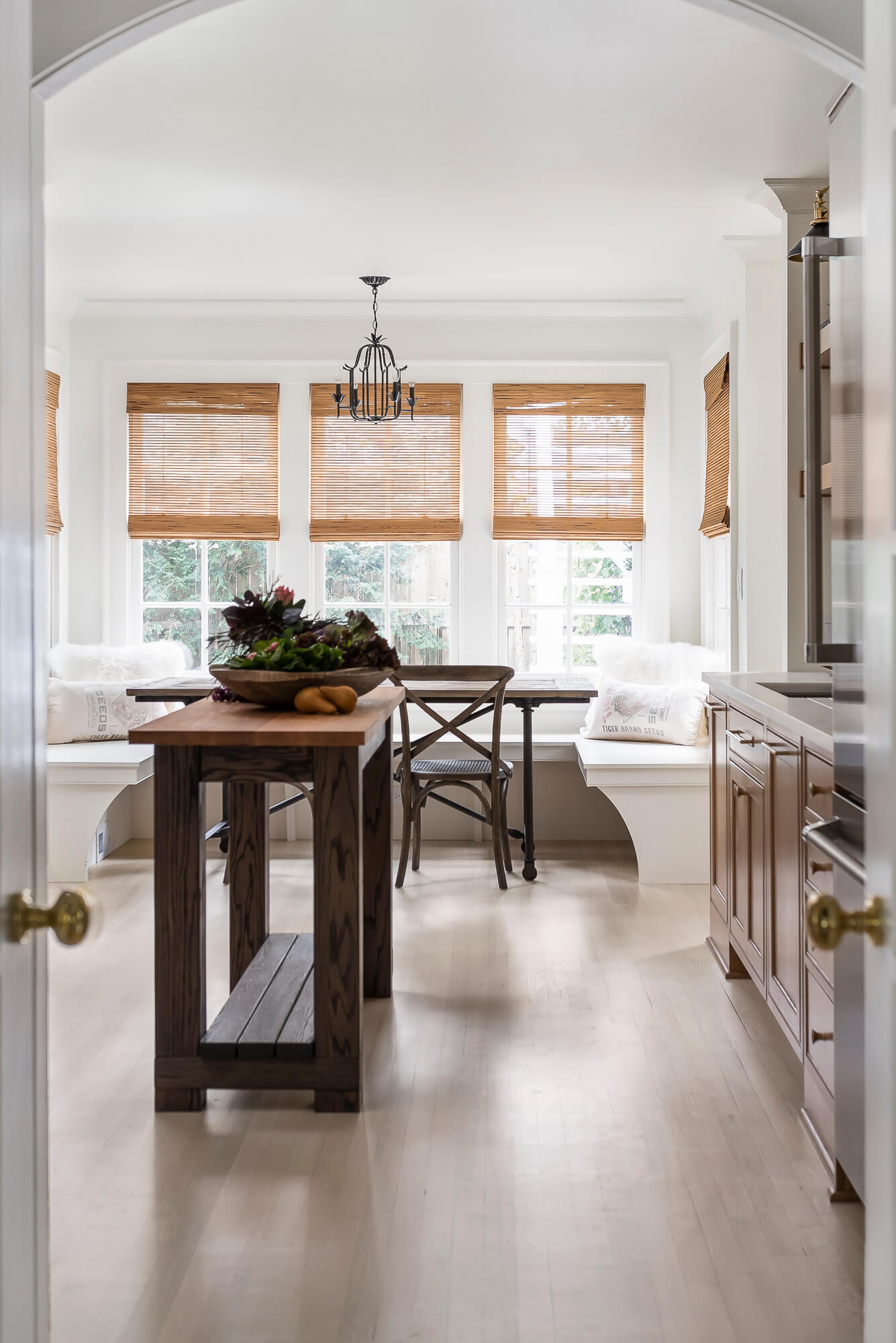 A look from the kitchen, over the small weathered kitchen island table into the dining room space with a bright white built-in breakfast nook with banquette seating.