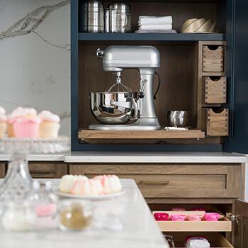 A countertop standing larder cabinet provides an orderly place to house appliances, like a large mixer. Thoughtfully planned shelves and cubbies provide dedicated space for an assortment of baking gadgets, pantry goods, and measuring cups, keeping them easy to find and at your fingertips. Explore more kitchen cabinet storage solutions and cabinet accessories from Dura Supreme Cabinetry.