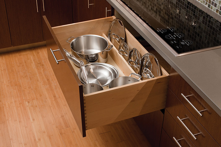 Kitchen storage ideas for around the cooking zone and cooktop area. A Lid Storage Partition from Dura Supreme placed at the back of a wide, deep drawer neatly stores pot and pan lids to keep your pot and pan storage orderly and easy to access.