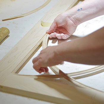 A close up of a cabinet maker's hands crafting the details of a decorative mullion kitchen cabinet door on a table.