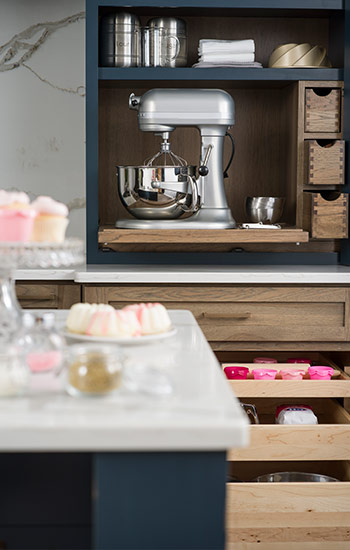 Kitchen cabinet storage trends. A navy blue and medium stained kitchen withlarder pantry cabinets designed for the perfect baking center.